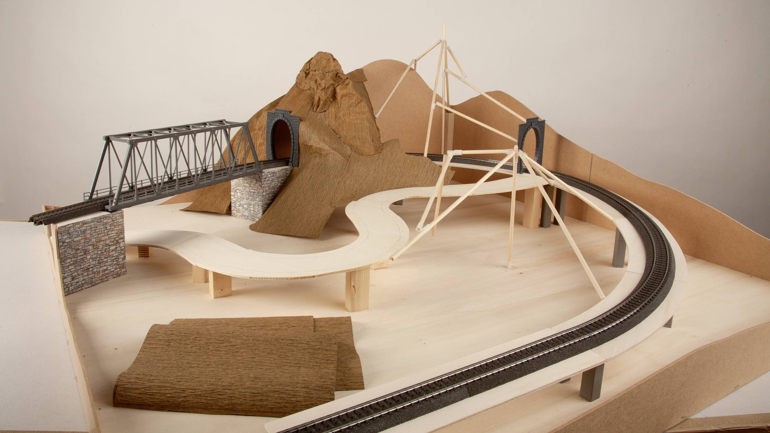 Model of a miniature railway landscape with bridges, a tunnel and a mountain made from cardboard and wood. Railway tracks run across the structure.