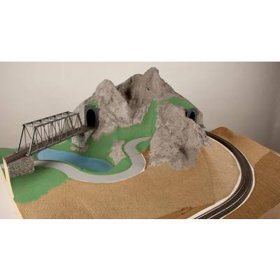 A model of a railway landscape with a bridge and two tunnels in a mountainous terrain, surrounded by a road and a pond.