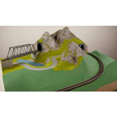 Model railway landscape with a tunnel, a bridge, a road and tracks winding around a hill.