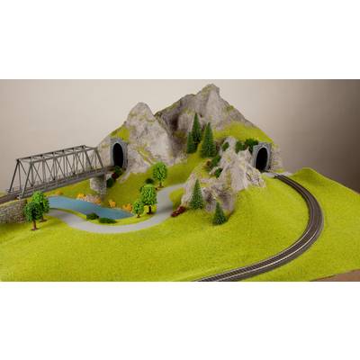 Model railway landscape with a bridge, two tunnels in hills, forest, meadows and railway tracks; shows a realistic miniature scene.