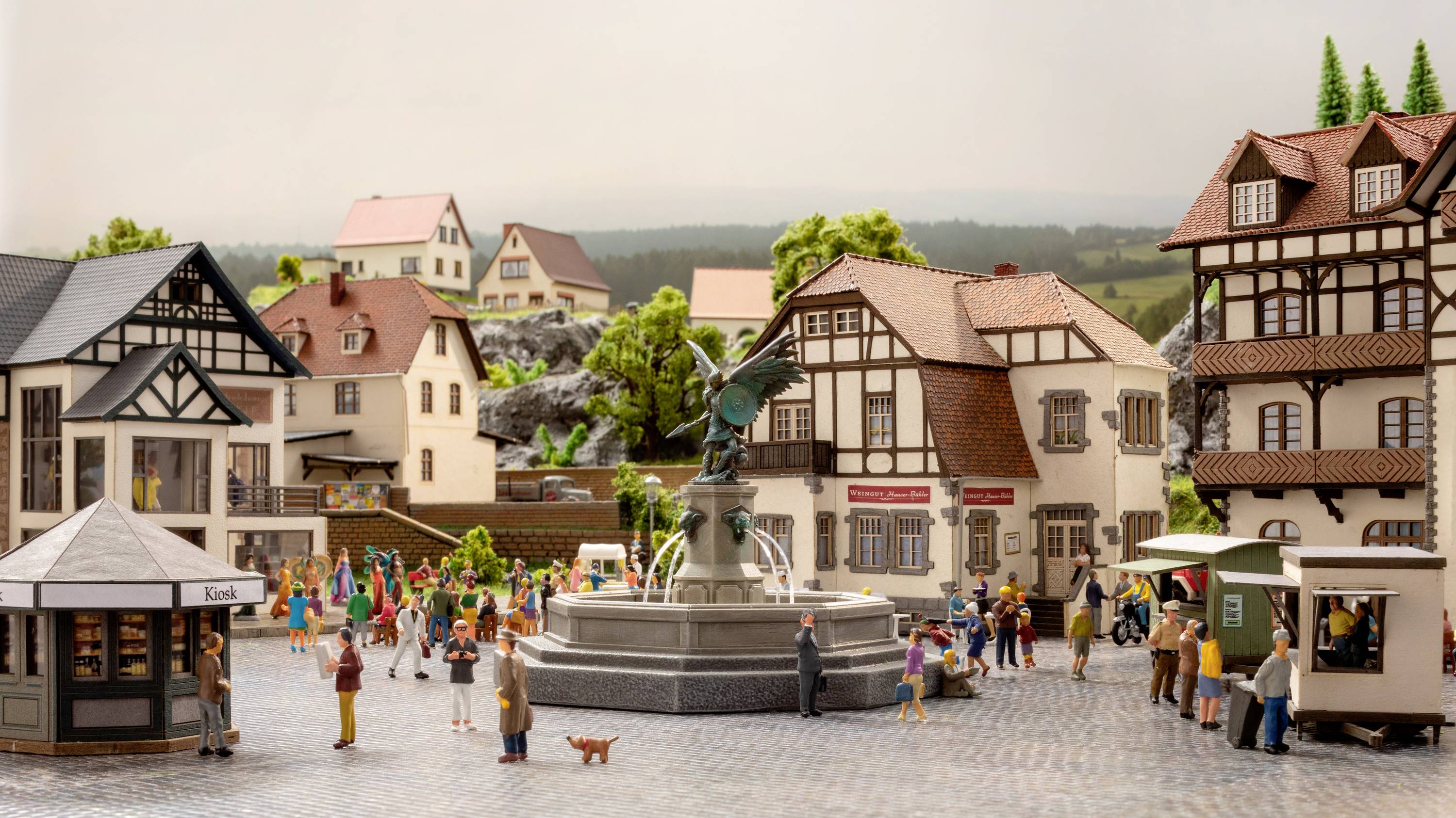 A bustling marketplace in a picturesque small town. People are strolling around a central fountain. Historic half-timbered houses surround the square.