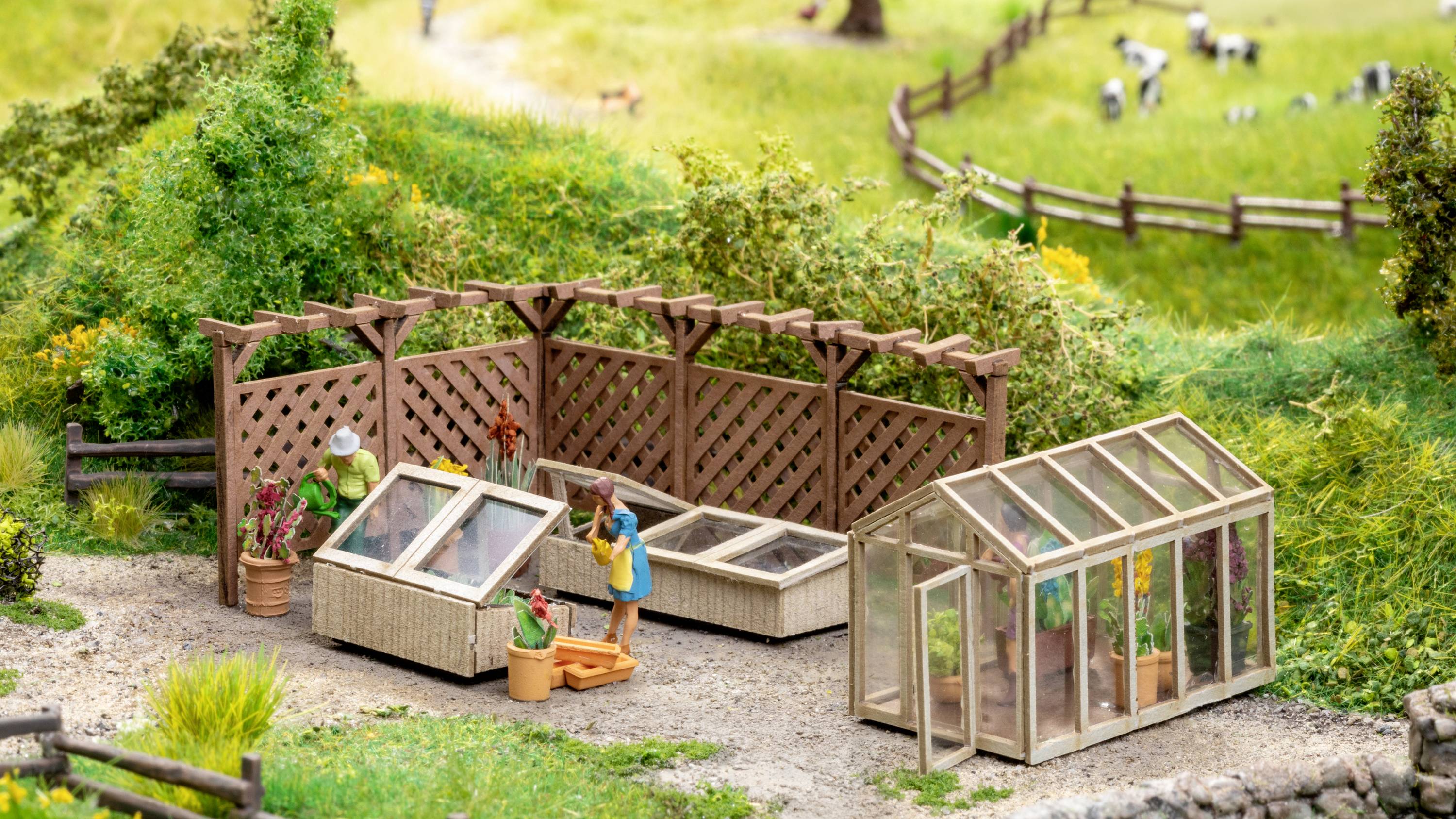 A miniature landscape depicts a greenhouse and people tending to plants. Fences and meadows can be seen in the background.