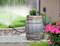 A water butt collects rainwater, which is used for watering a garden with lawn and flowers. A sprinkler distributes the water.
