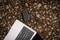 A laptop is resting on a gravel surface. A black cable is connected and leads to an external device beside the laptop.