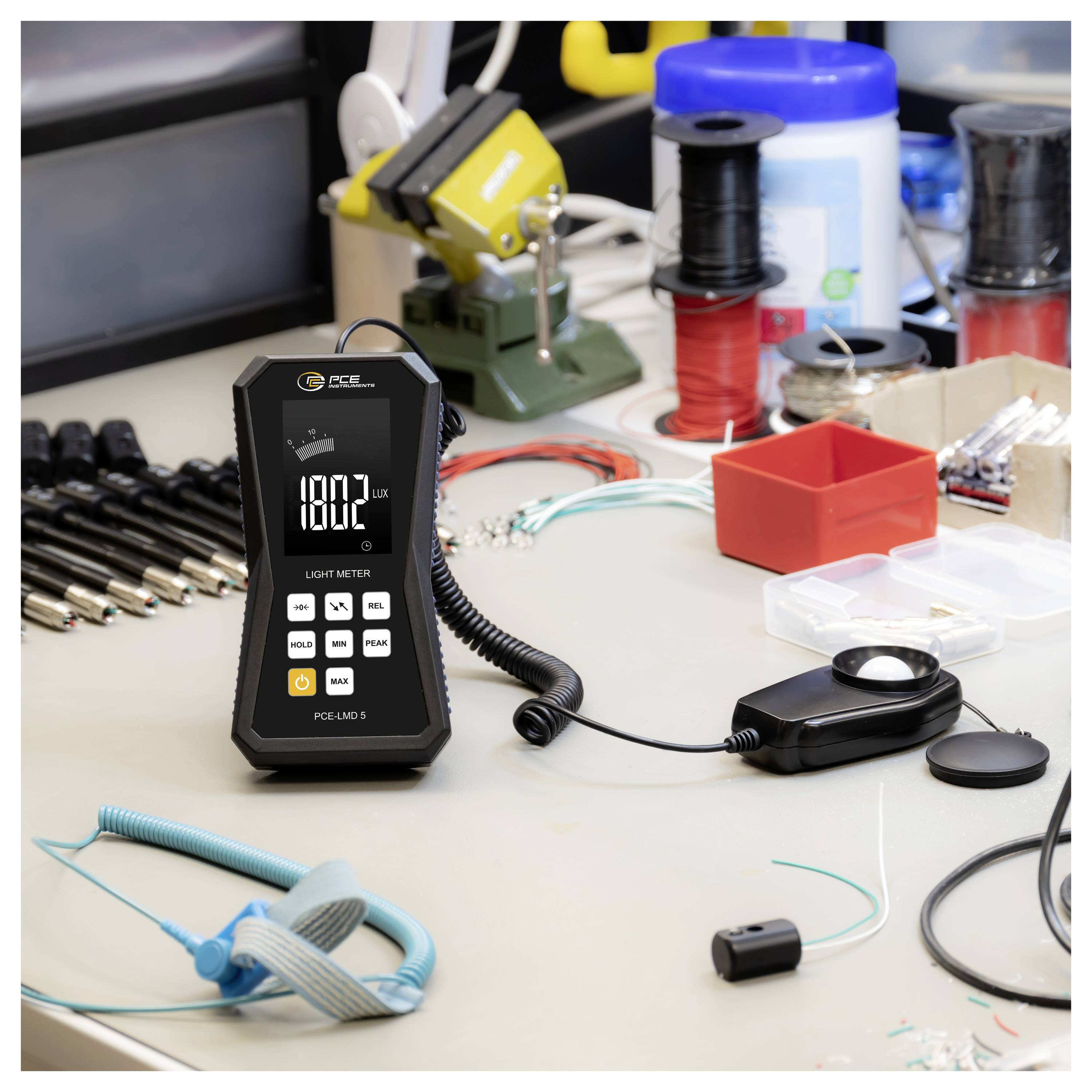 Light meter on a workbench displays 1802 lux, with a sensor probe, wires, and small electronics tools scattered around.