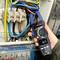 A person is using a digital multimeter to measure voltages on an electrical control panel. Colourful cables are visible.