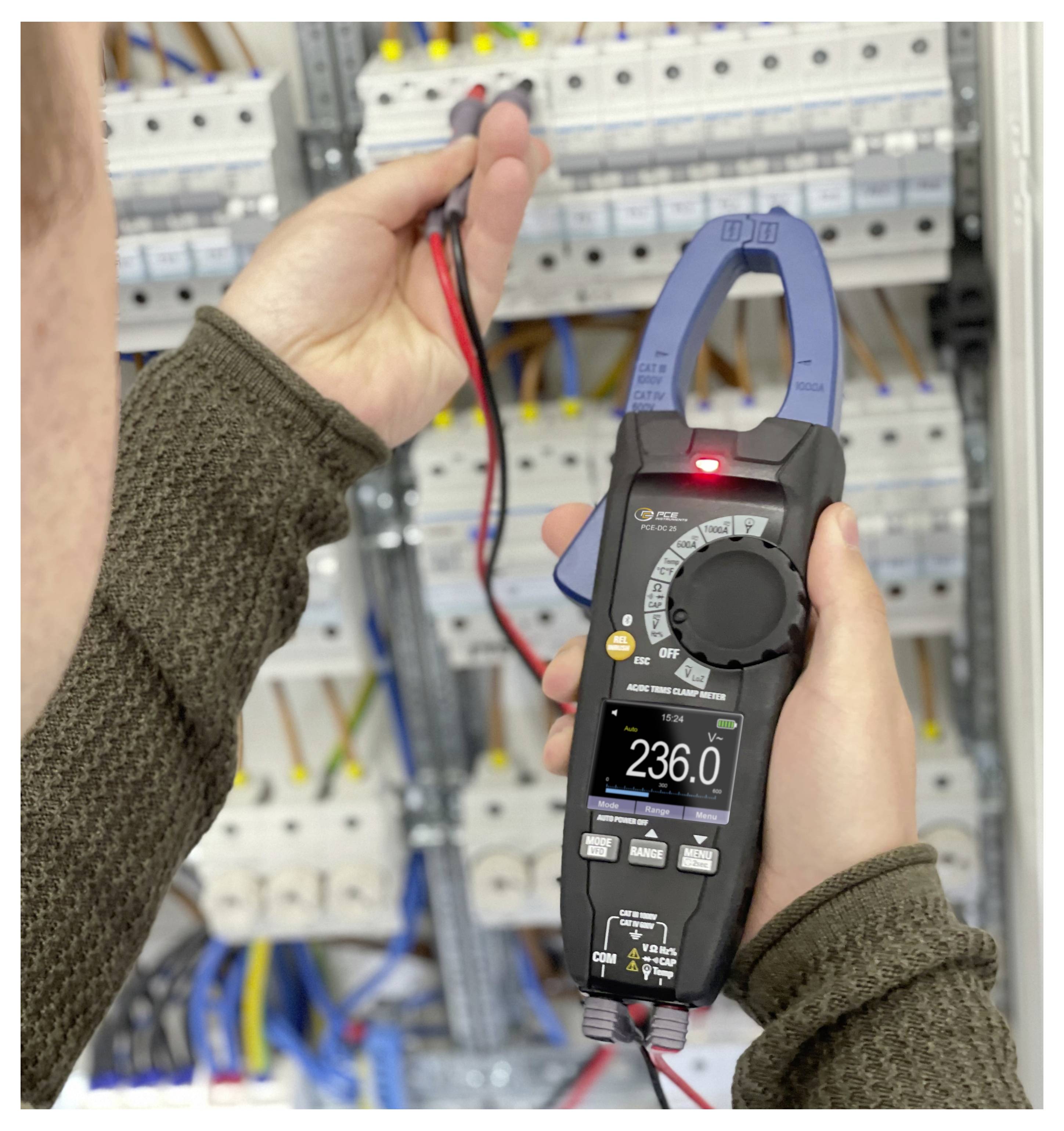 Person using a clamp meter to test electrical wiring in an open circuit panel; the meter display reads 236.0 V.