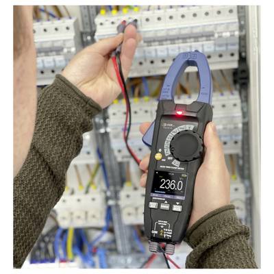 Person using a clamp meter to test electrical wiring in an open circuit panel; the meter display reads 236.0 V.