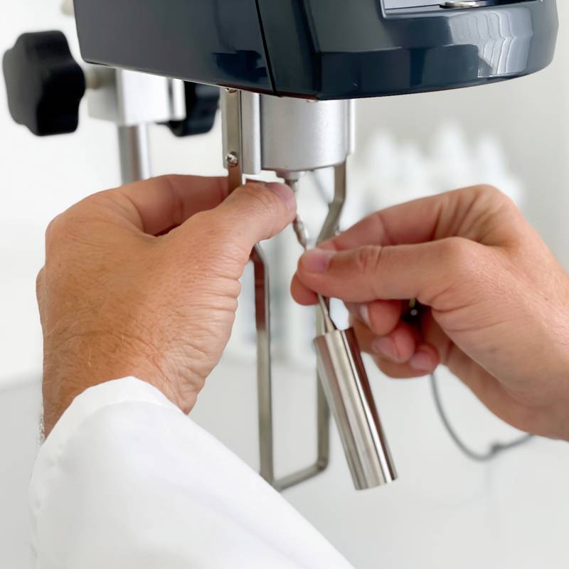 A person is operating an espresso machine and holding the portafilter. Hands are visible in a bright, clean room.