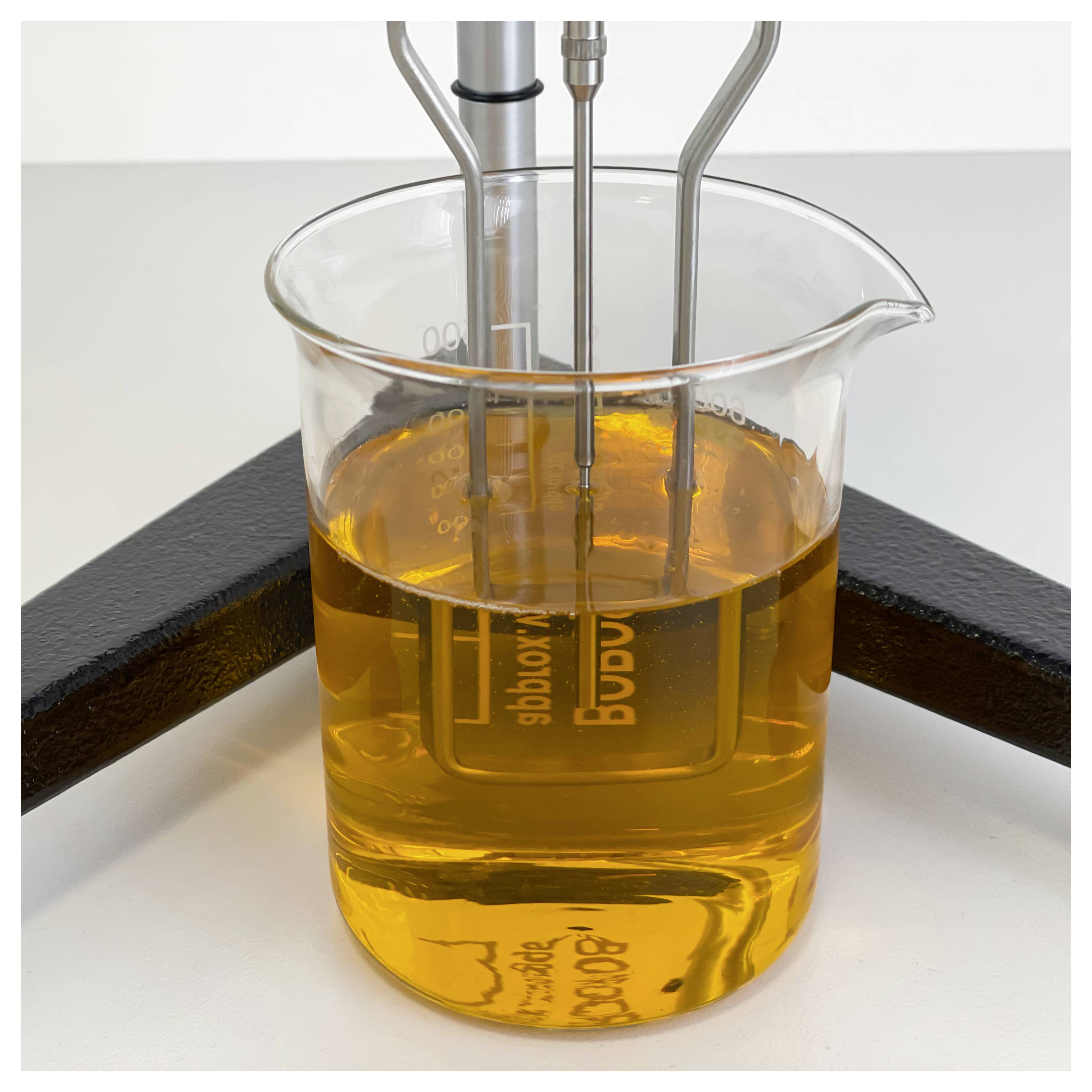 Laboratory beaker of amber liquid with immersed probes or electrodes, shown in a scientific measurement setup on a benchtop.