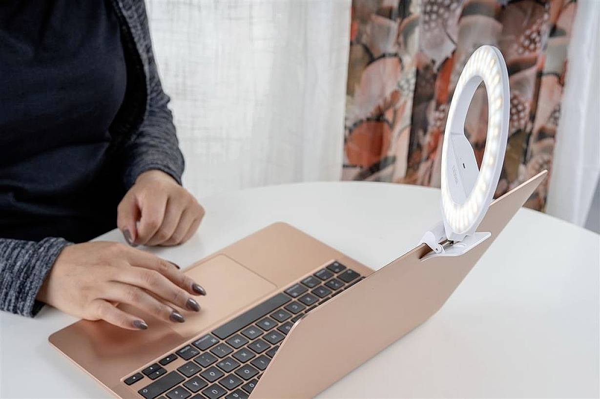 A person is typing on a laptop with a ring light attached.