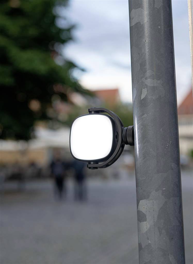Street lamp light cover outdoors, with a blurred background of trees and people walking past.