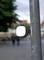 Street lamp light cover outdoors, with a blurred background of trees and people walking past.
