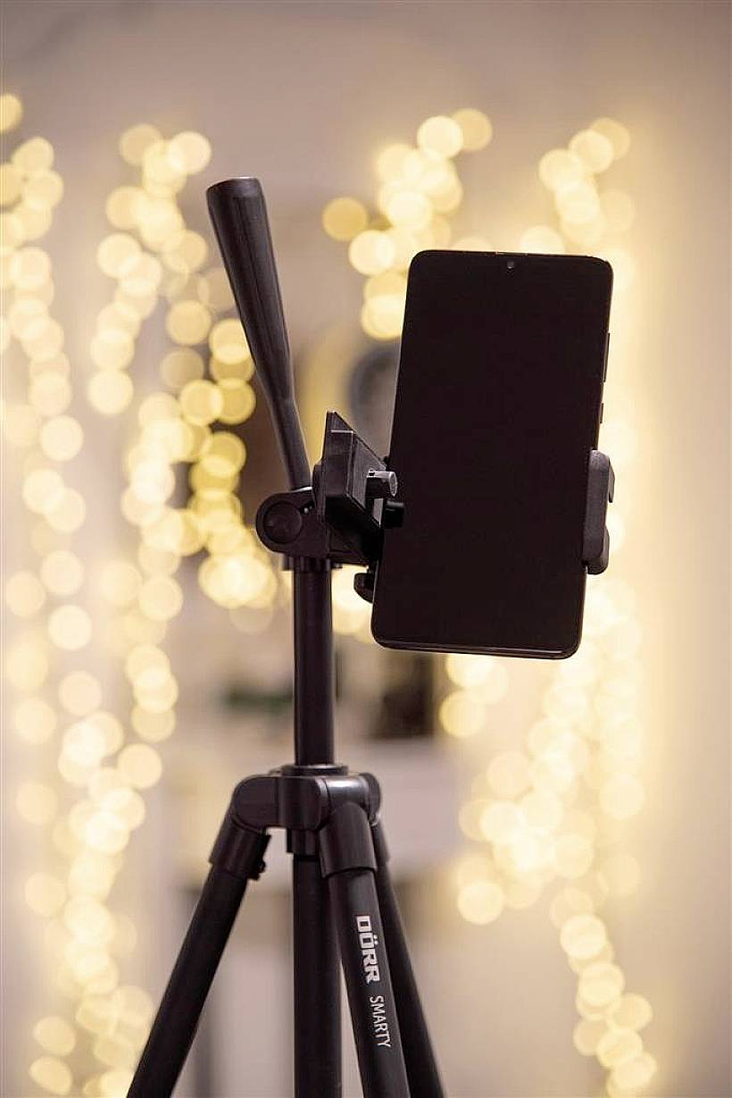 A tripod holds a smartphone; blurred lights in the background create a warm and cosy atmosphere.