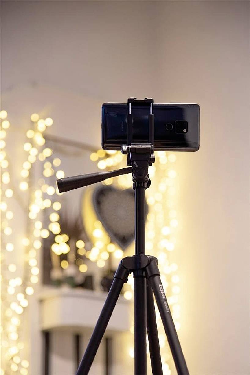 A smartphone is mounted on a tripod. In the background, out-of-focus, warm lights can be seen creating a cosy atmosphere.