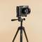A black camera on a tripod against a beige background.