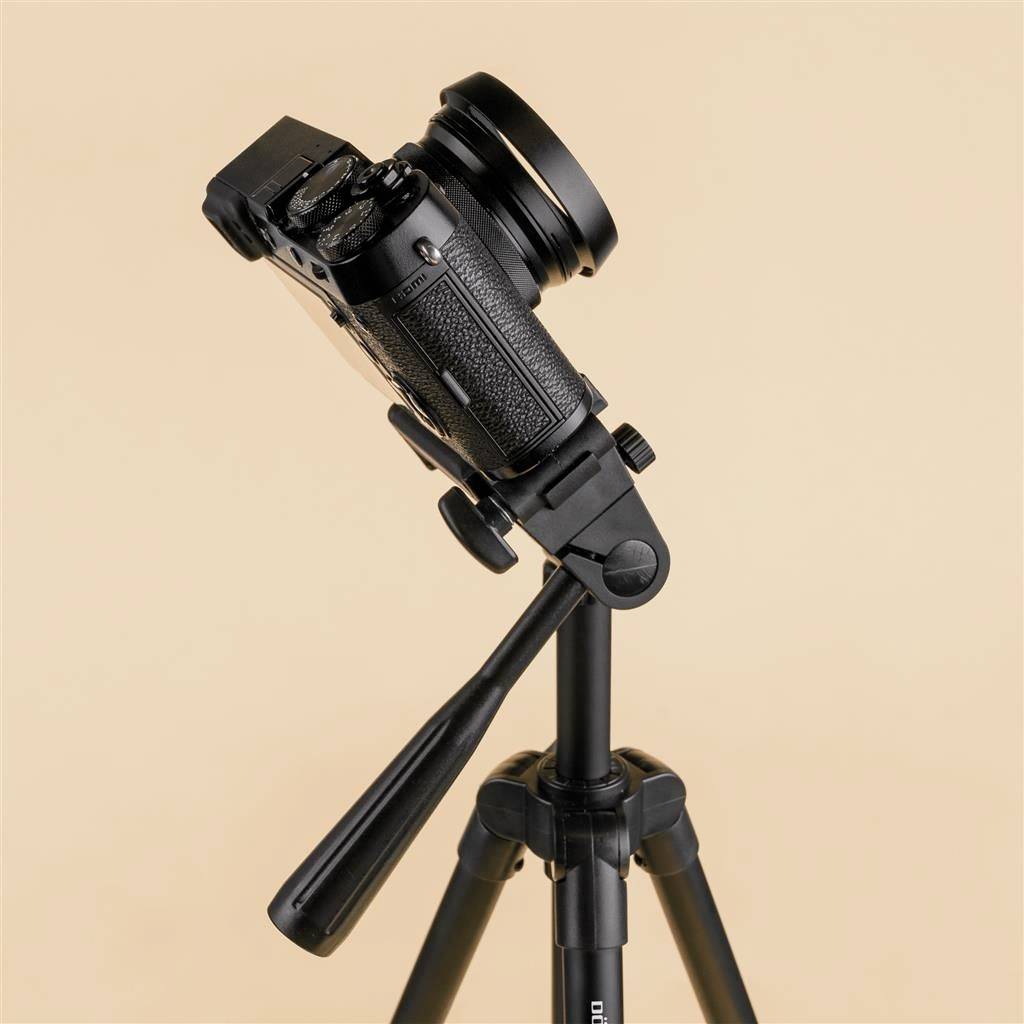 A black camera on a tripod, tilted to the side, against a plain, beige background.