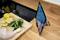 A tablet is standing on a kitchen worktop, displaying a recipe. Beside it lies a chopping board with lemons, herbs, and a chicken leg.