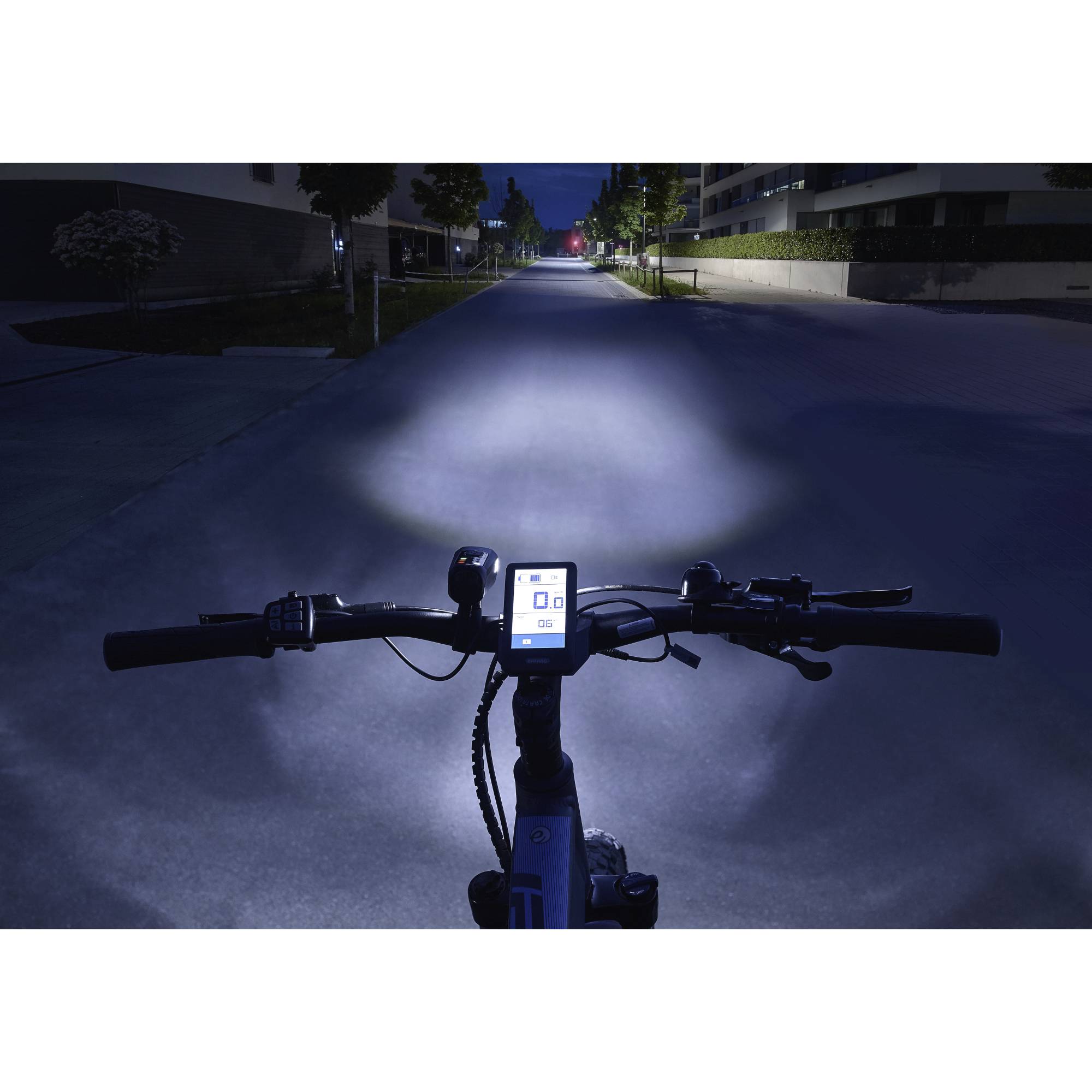 View from a cyclist's perspective at night on a lit street; e-bike display showing speed and battery indicator.