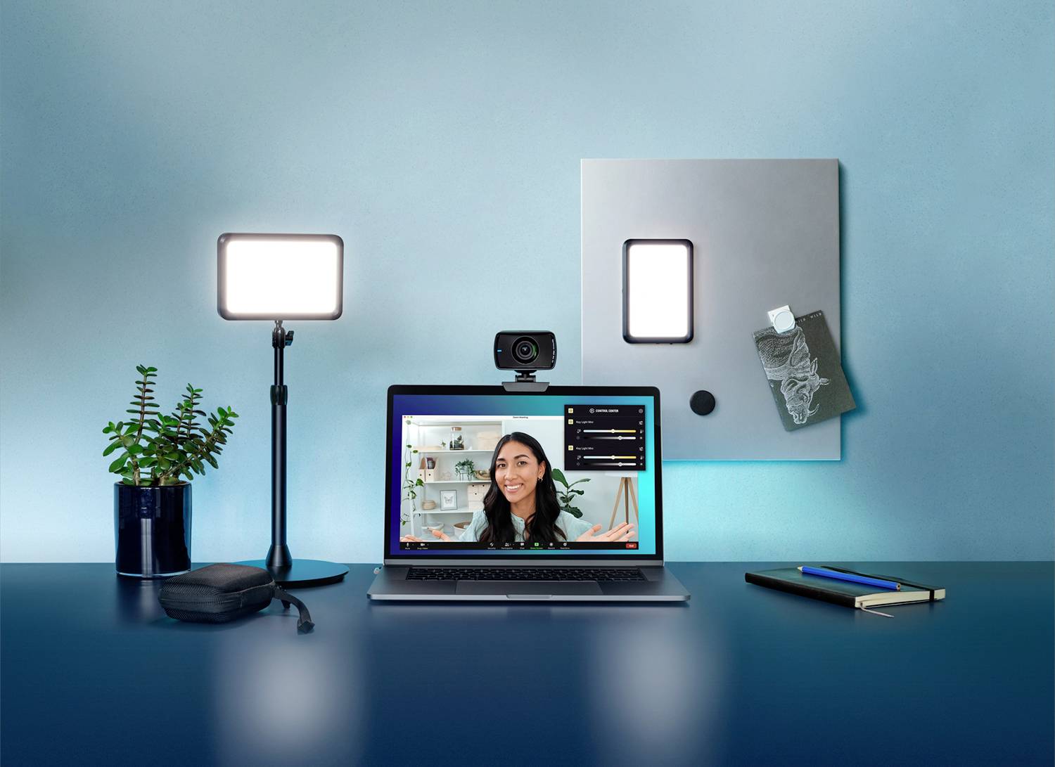 Workstation with a laptop showing a video call, illuminated by a lamp. Webcam positioned at the top of the laptop. Accessories and plants nearby.