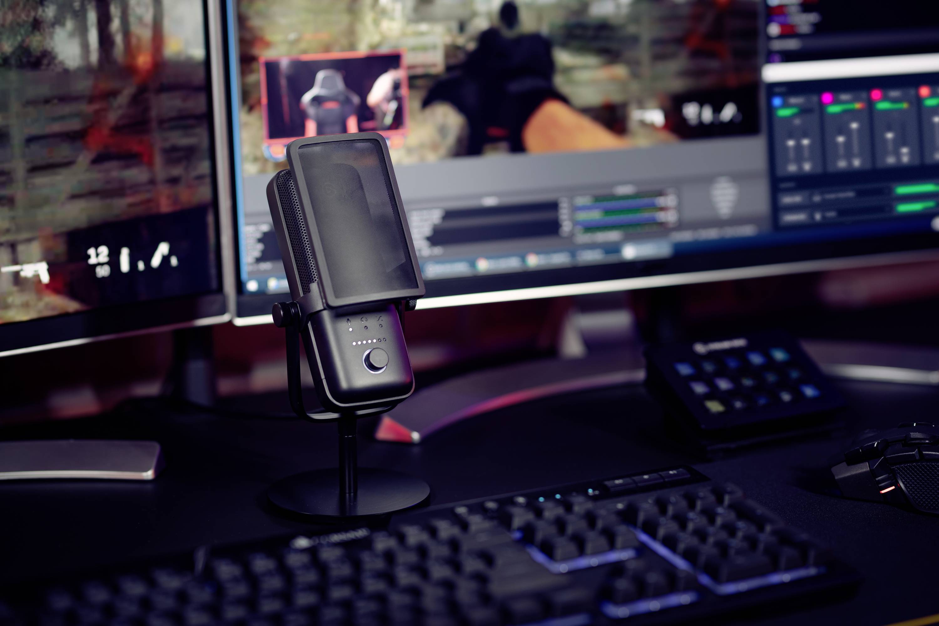 A computer workstation with two monitors, a microphone, a keyboard and streaming software. A game is running on the screens.