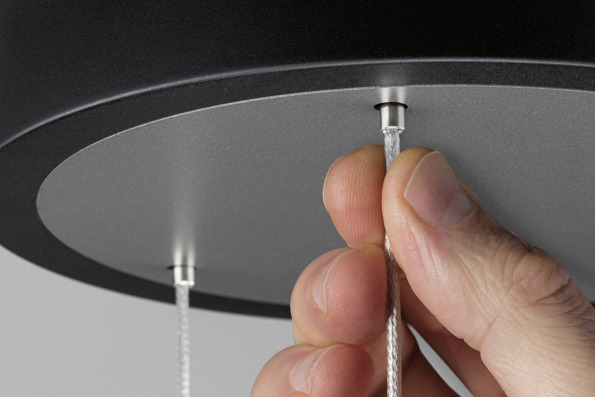 A hand pulls on a thin cable of a black lamp from below. The scene shows a view of the lamp adjustment mechanism.