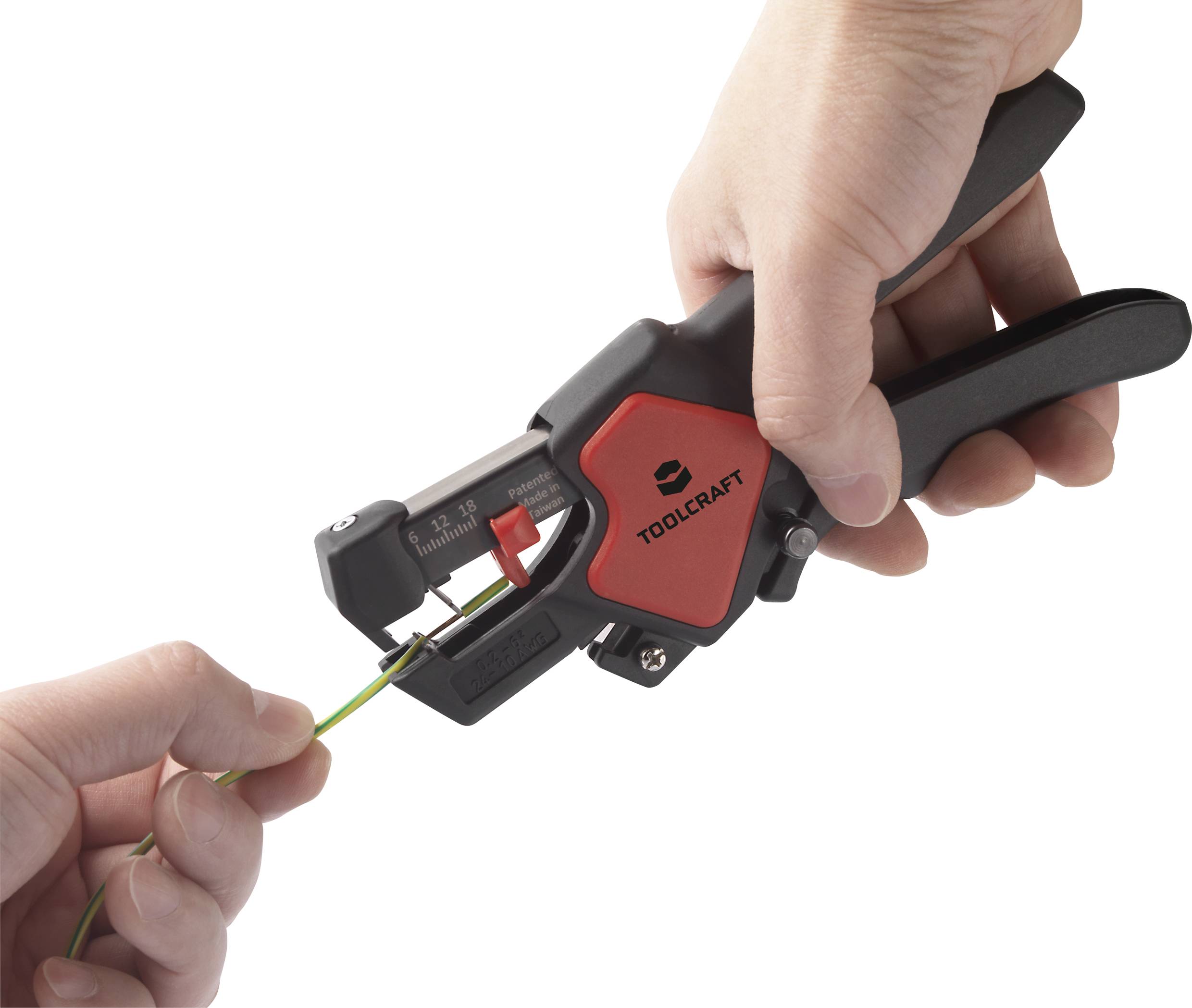 Two hands are holding a wire stripper to strip a green cable. The wire stripper is black with a red section and the brand 'Toolcraft'.