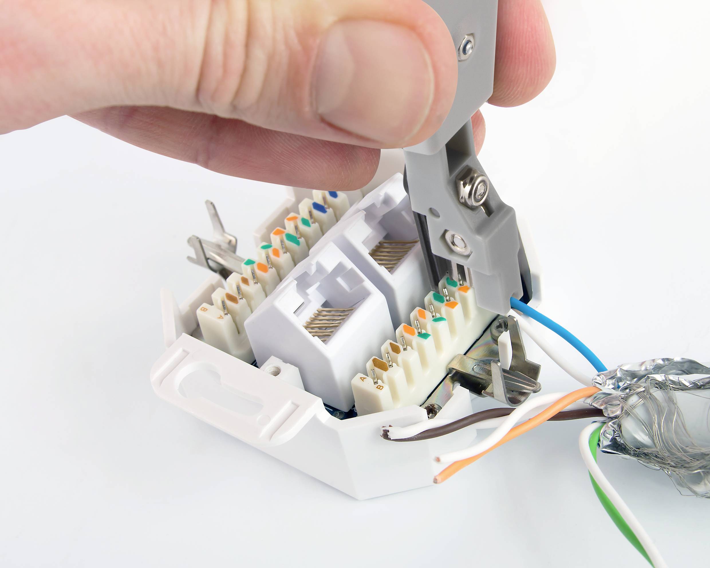 A hand uses a tool to insert cables into a network terminal. Several colourful cables are visible.