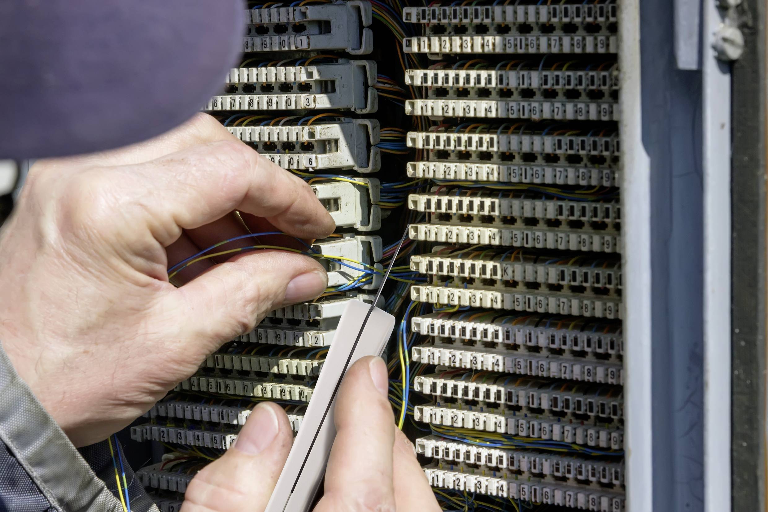 A person is working on a cable connection box, connecting or disconnecting wires. The focus is on the hands and the cables.