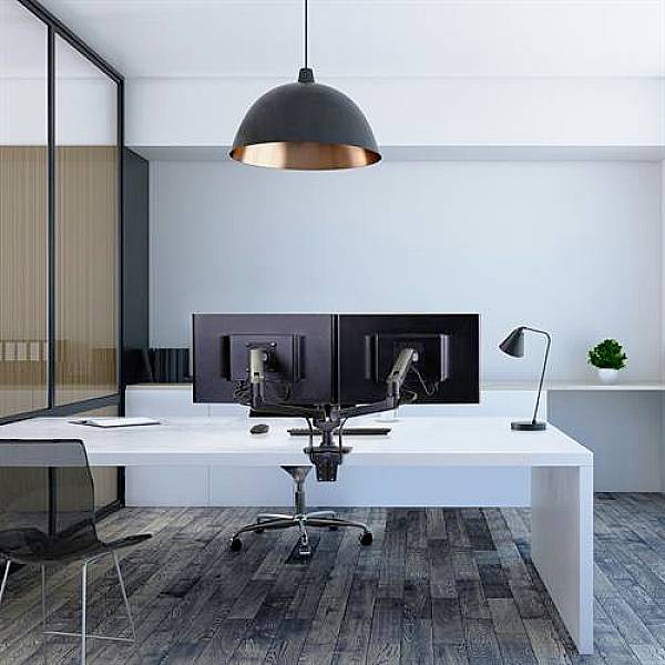 A modern office with two monitors on a desk, a pendant light hanging above, and a small plant arrangement to the right.