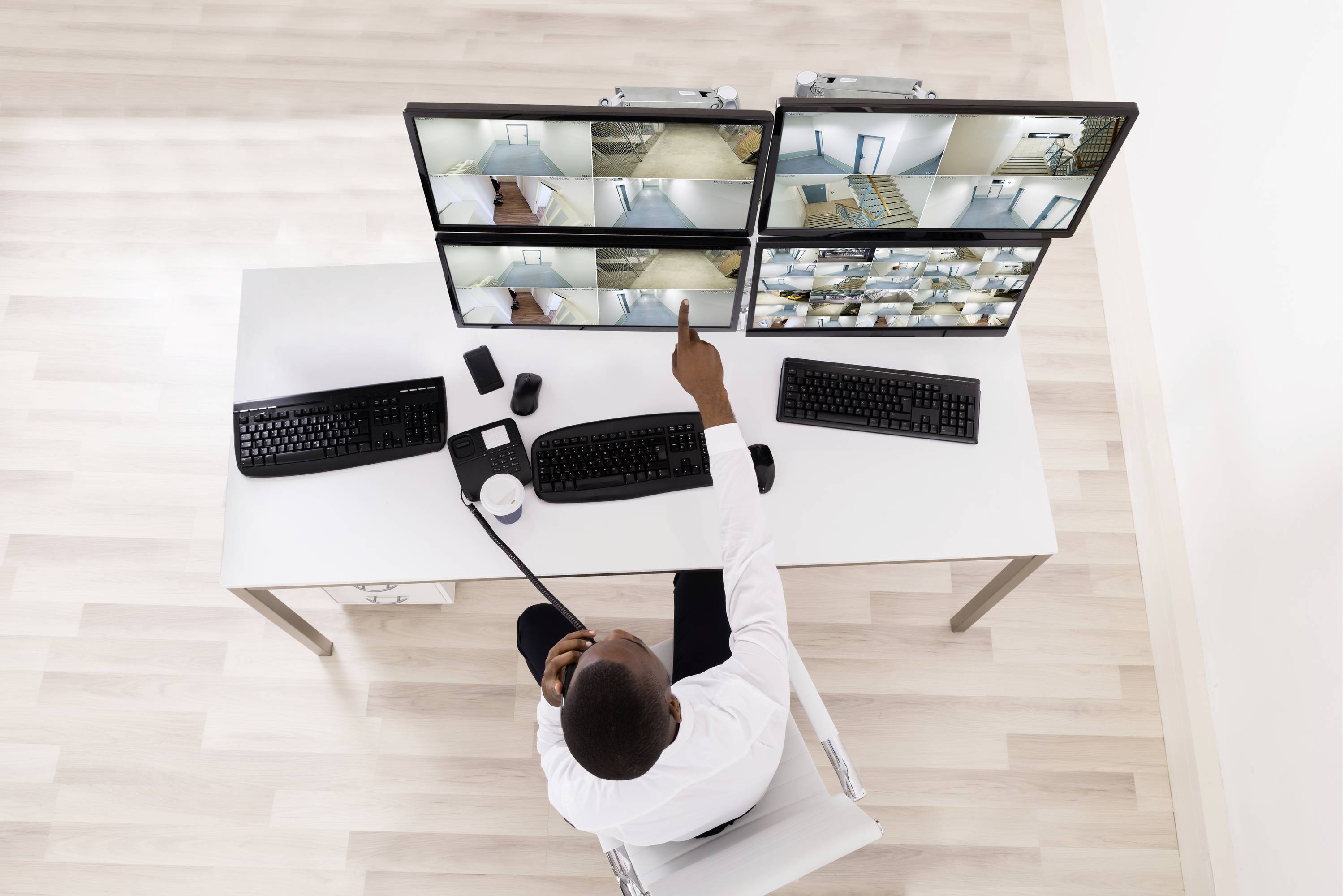 A person is monitoring multiple surveillance cameras on screens in an office. They are using a walkie-talkie.