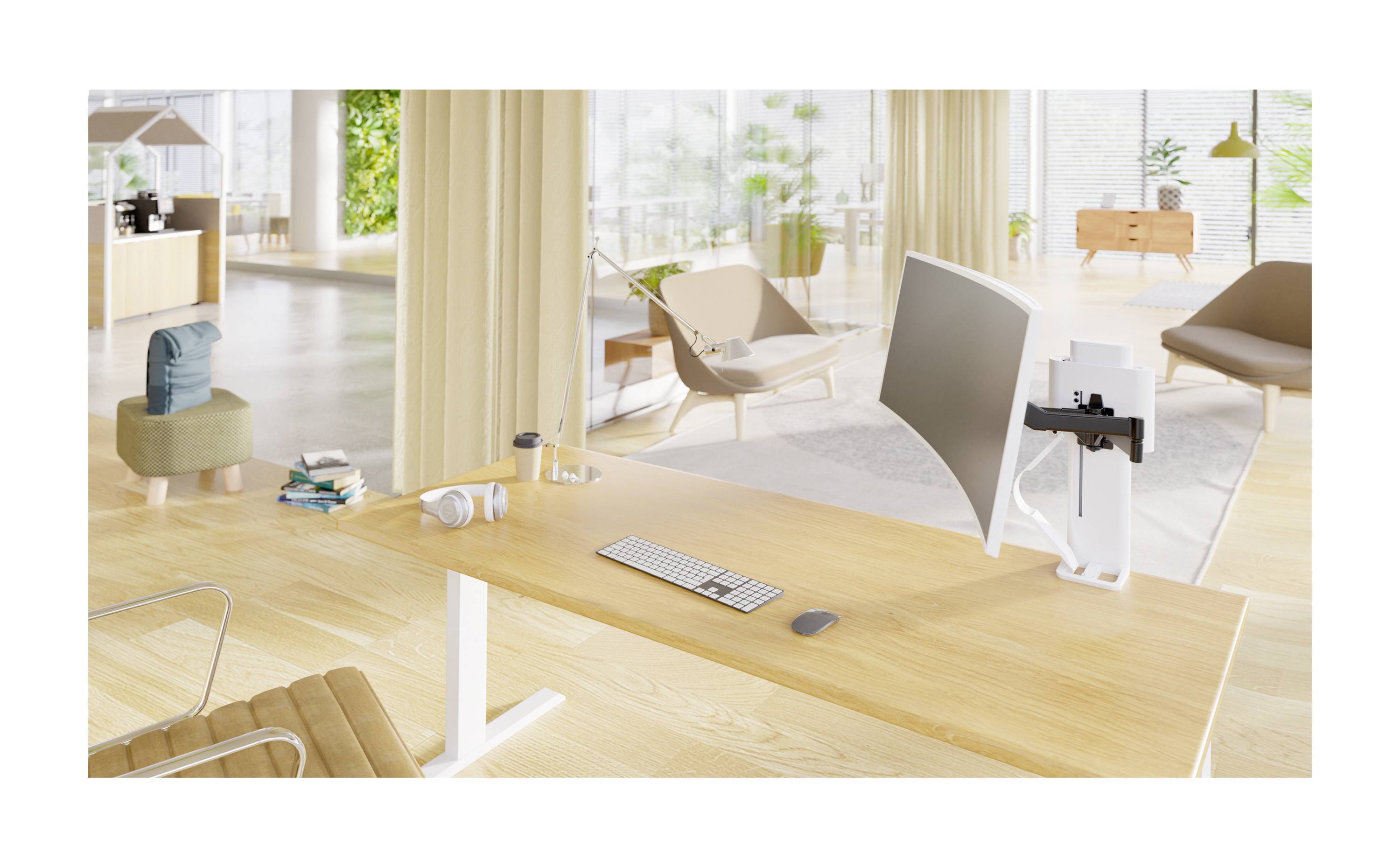 Modern office space with a desk, featuring a monitor, keyboard, and mouse. In the background, seating areas and large plants are visible.