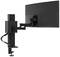 A black monitor mounting arm holds a large screen attached to a table. The arm is flexibly adjustable.