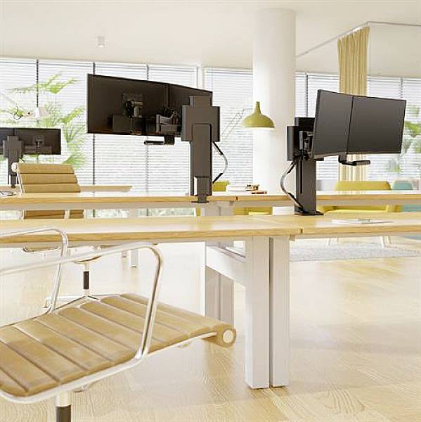 Office with contemporary desks and monitor arms, empty chairs and large windows that allow plenty of natural daylight to enter.