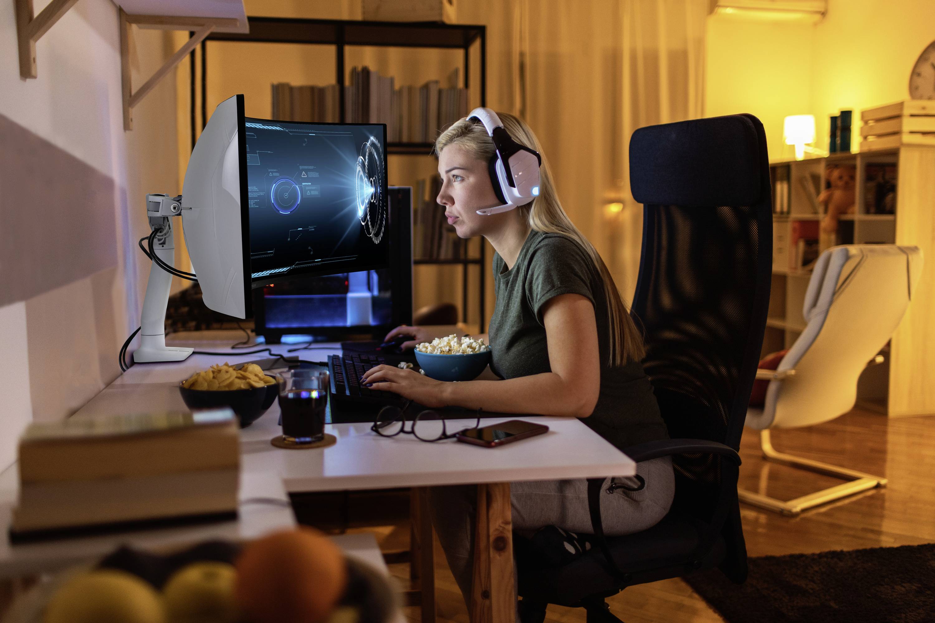 A person is sitting at a computer wearing a headset. Futuristic graphics are displayed on the screen. The environment appears cosy.