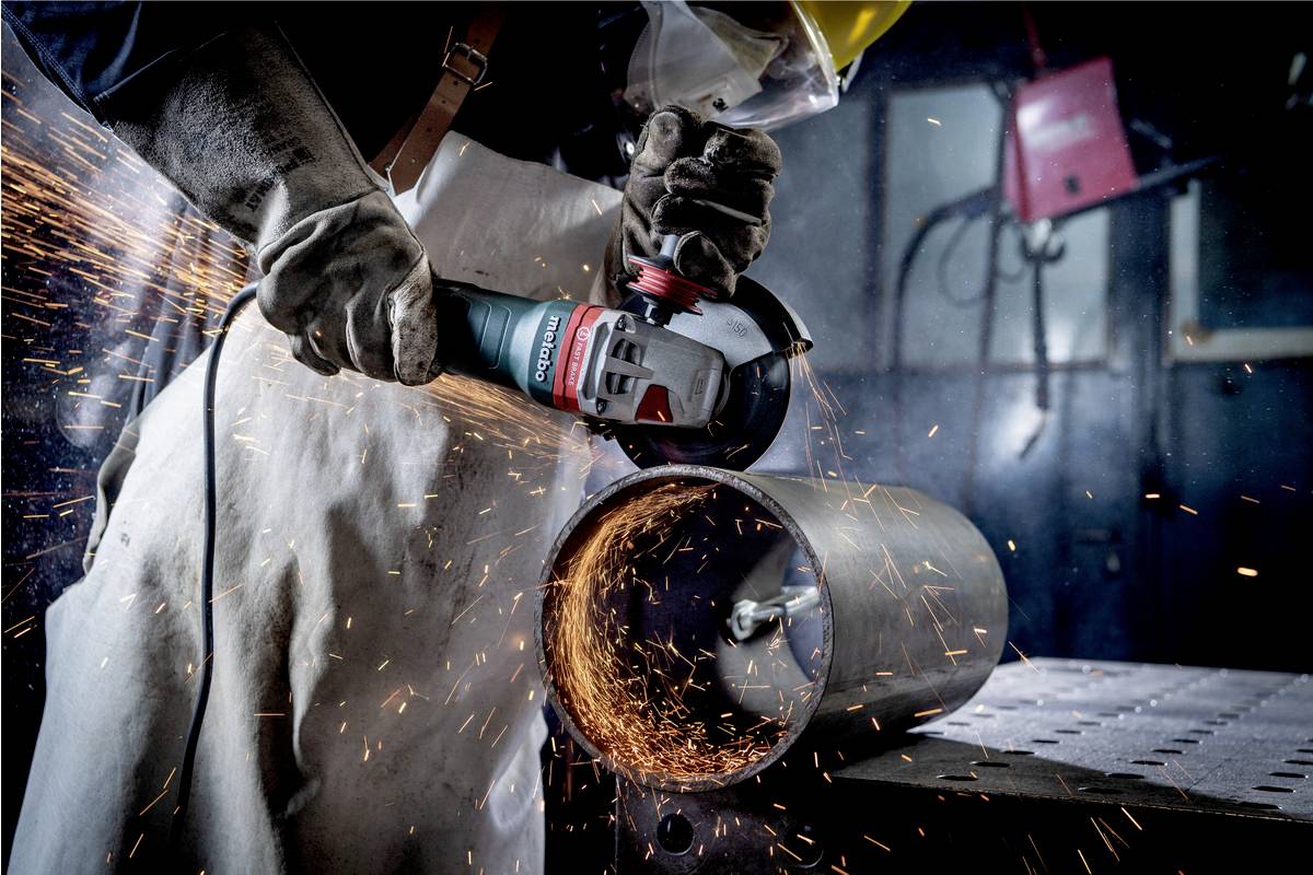 A person is grinding a metal pipe with an angle grinder while sparks are flying. They are wearing protective clothing and gloves.