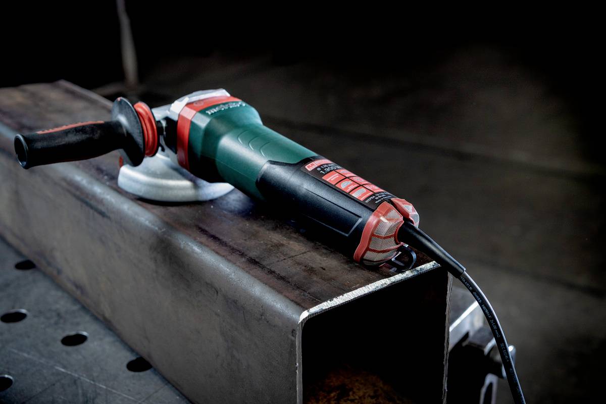 A green electric angle grinder is resting on a metal stand on a workshop bench.