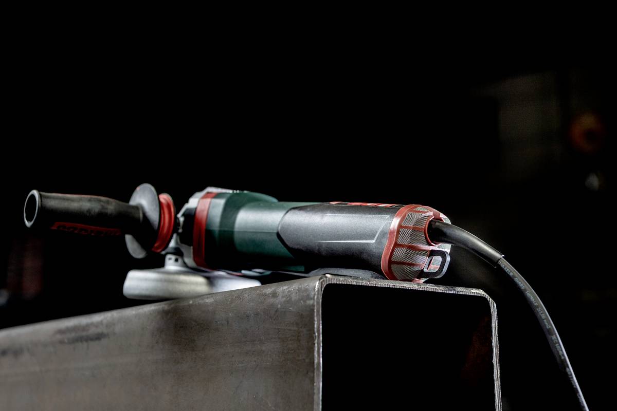 An angle grinder machine is resting on a large metal support. The background is dark, with the focus on the tool.