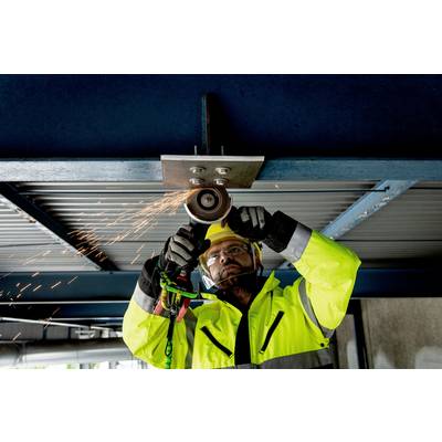 A construction worker in yellow protective clothing is using an angle grinder to process metal beams. Sparks are spraying downwards.