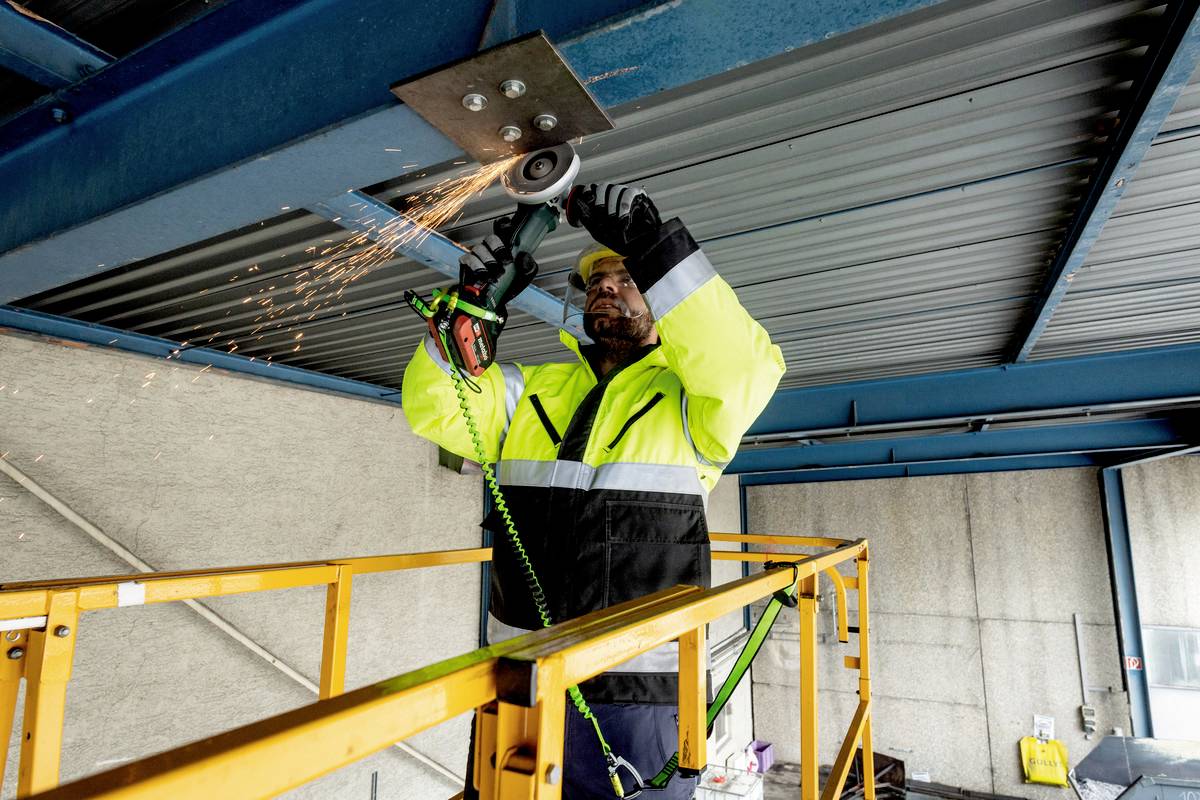 A person is working with an angle grinder on a metallic structure on scaffolding. Sparks are flying from the point of processing.