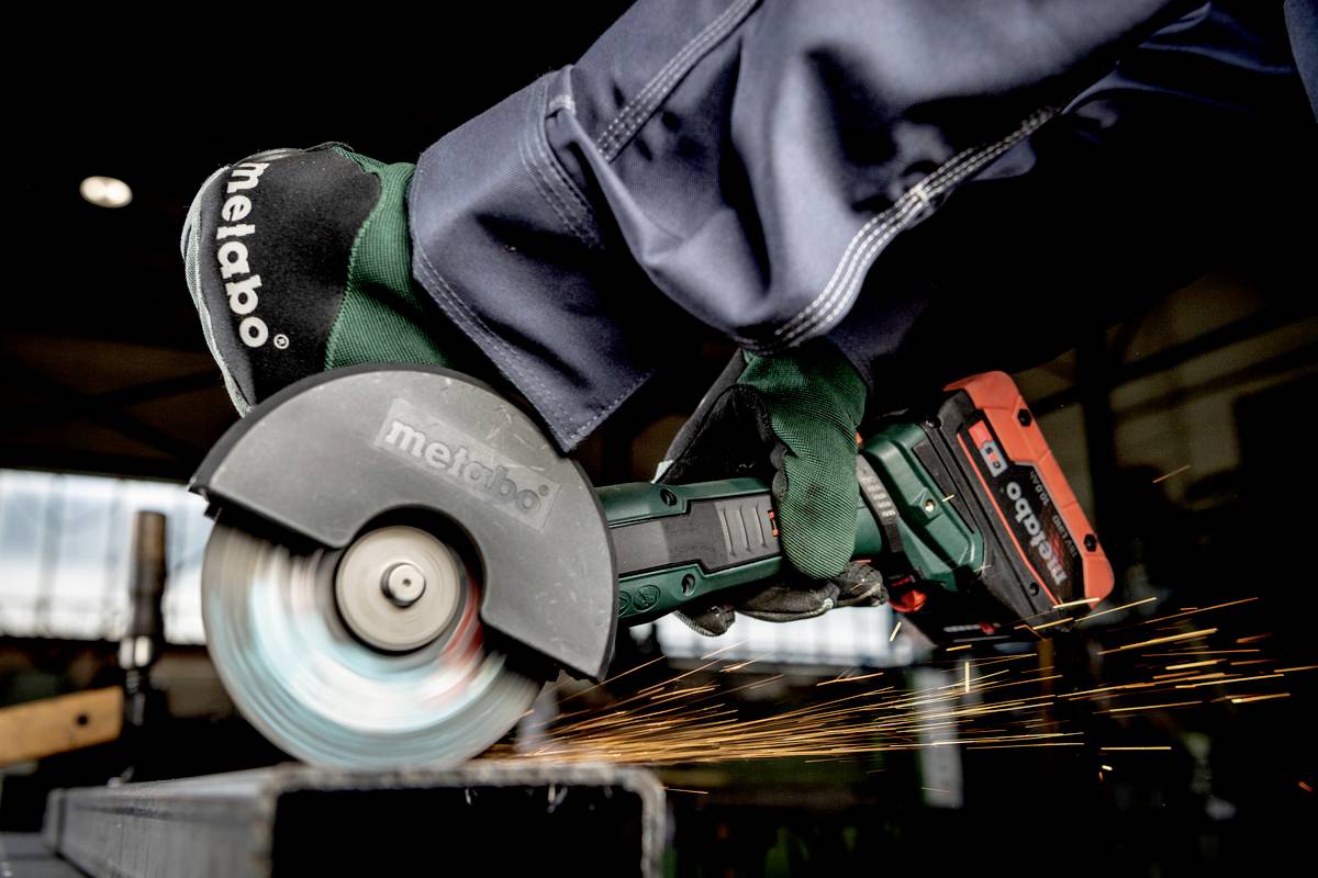 A worker is using an angle grinder to cut a metal element. Sparks are flying in a workshop.