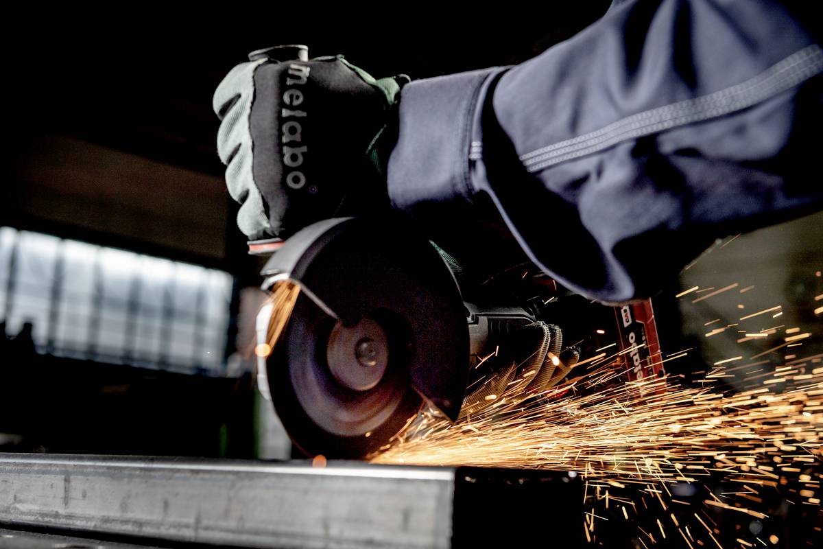 A worker wearing protective gloves grinds a piece of metal, with sparks flying.