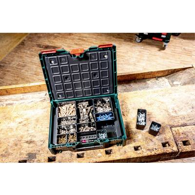 An open toolbox contains sorted screws, wall plugs and nails. It is sitting on a workbench in a workshop environment.