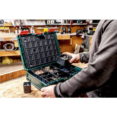 A person is sorting screws and nails in a green organiser case on a workbench in a well-equipped workshop.