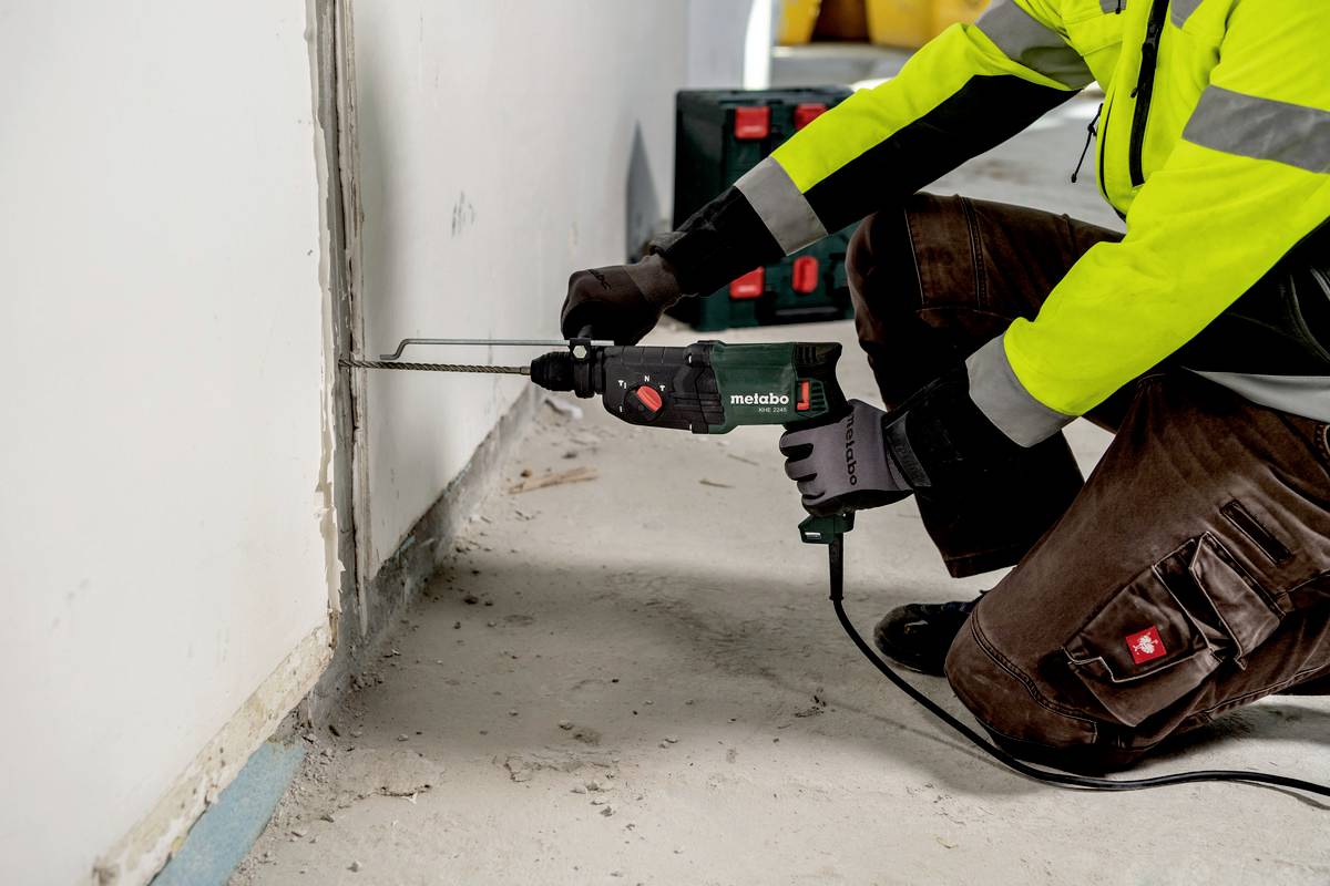 A person wearing safety clothing is using an electric saw to cut a slot in a white wall.