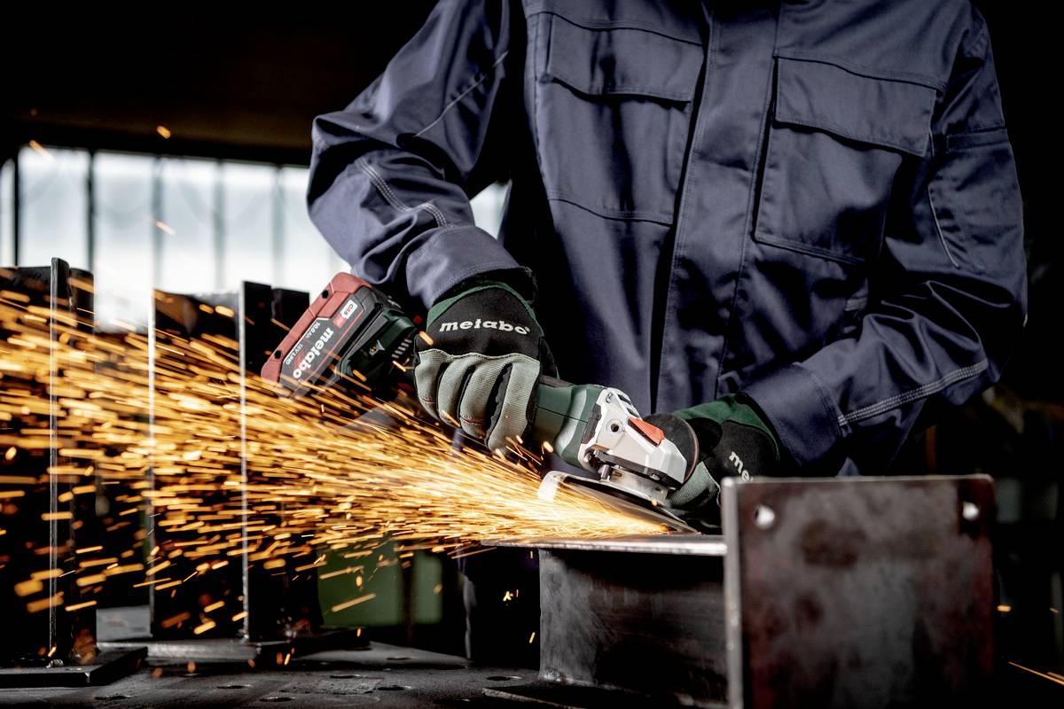 A person is grinding metal with an electric grinding machine. Sparks are flying off the metal surface. The person is wearing protective clothing.