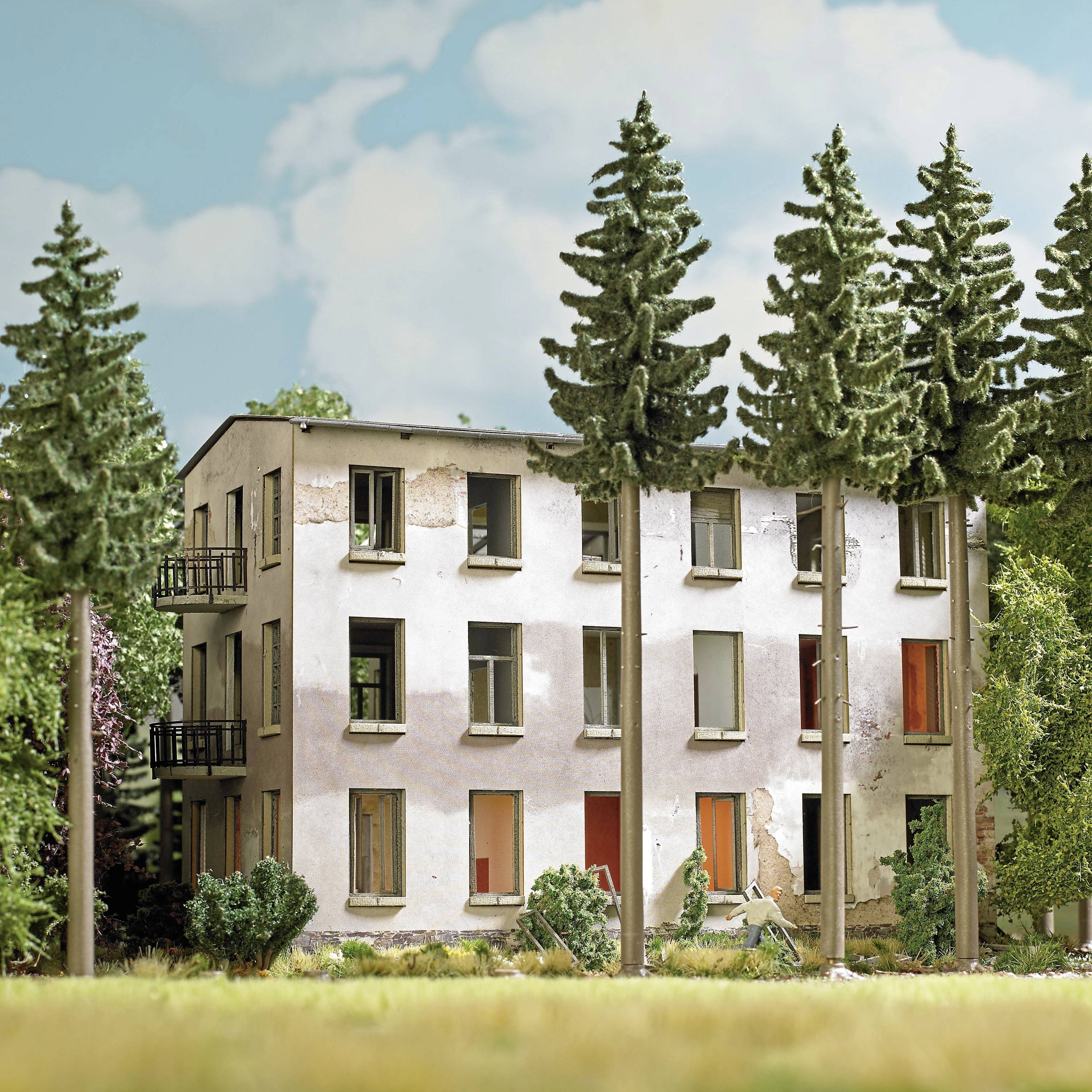 A three-storey, dilapidated building with damaged facades and windows, surrounded by tall, slender trees.