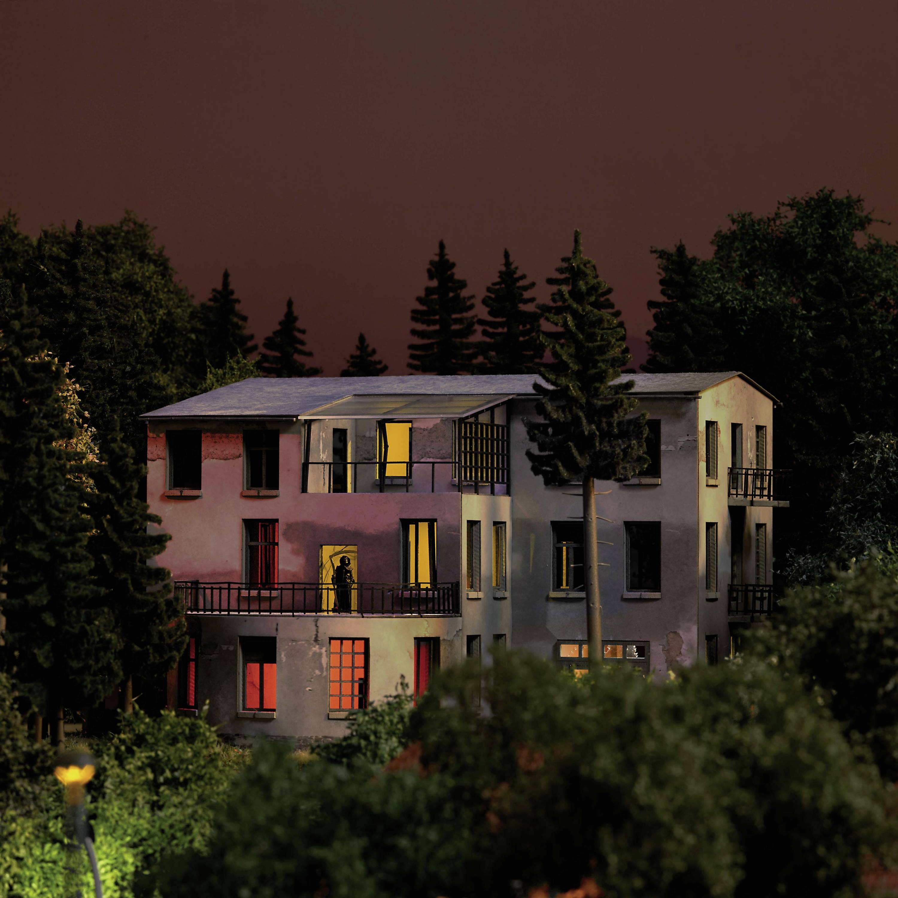 A lit-up house at dusk, surrounded by trees. Various windows emit warm light.