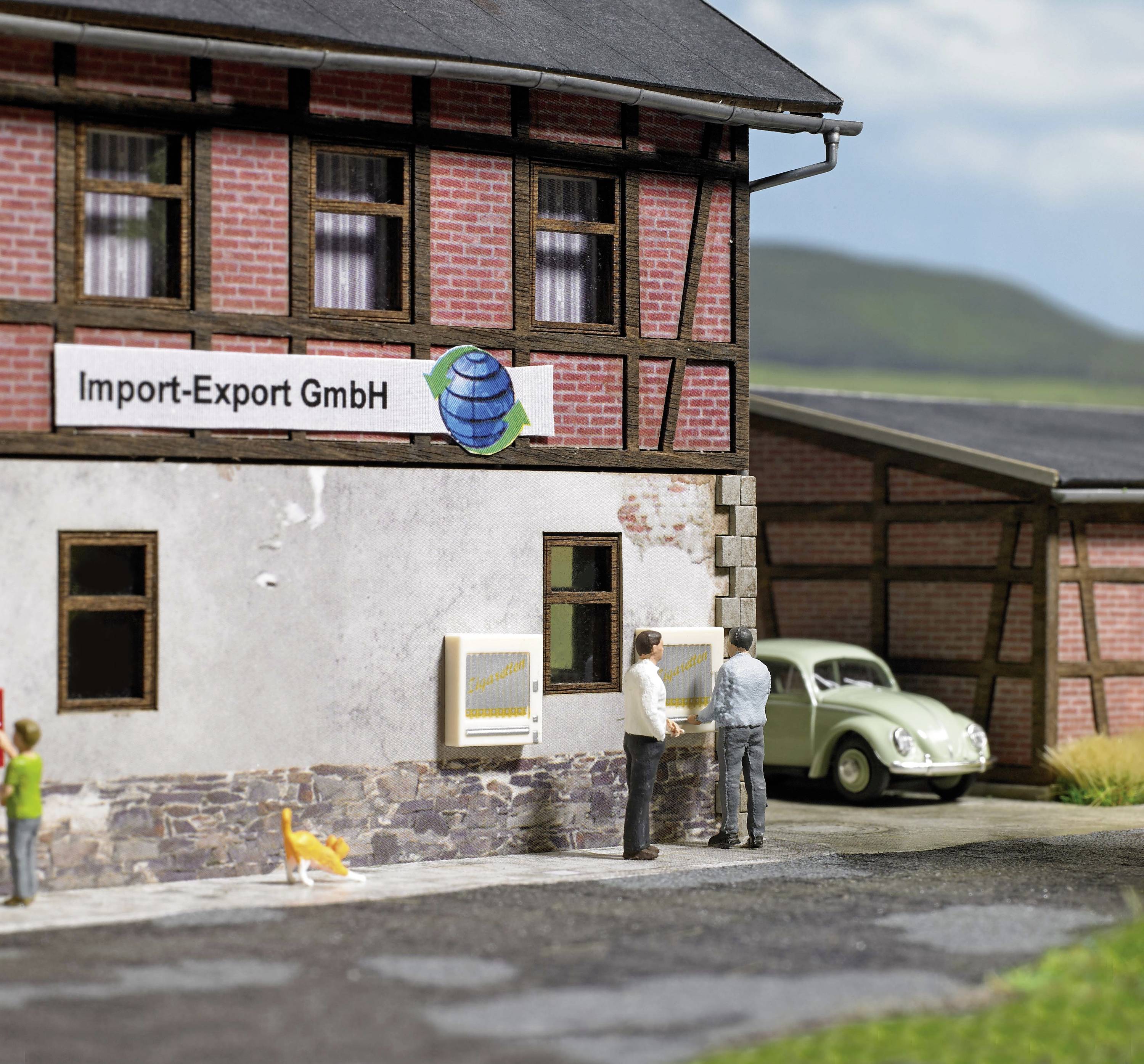 A model building with a sign reading 'Import-Export Ltd'. Two people and a dog are standing in front of it. A green car is in the background.