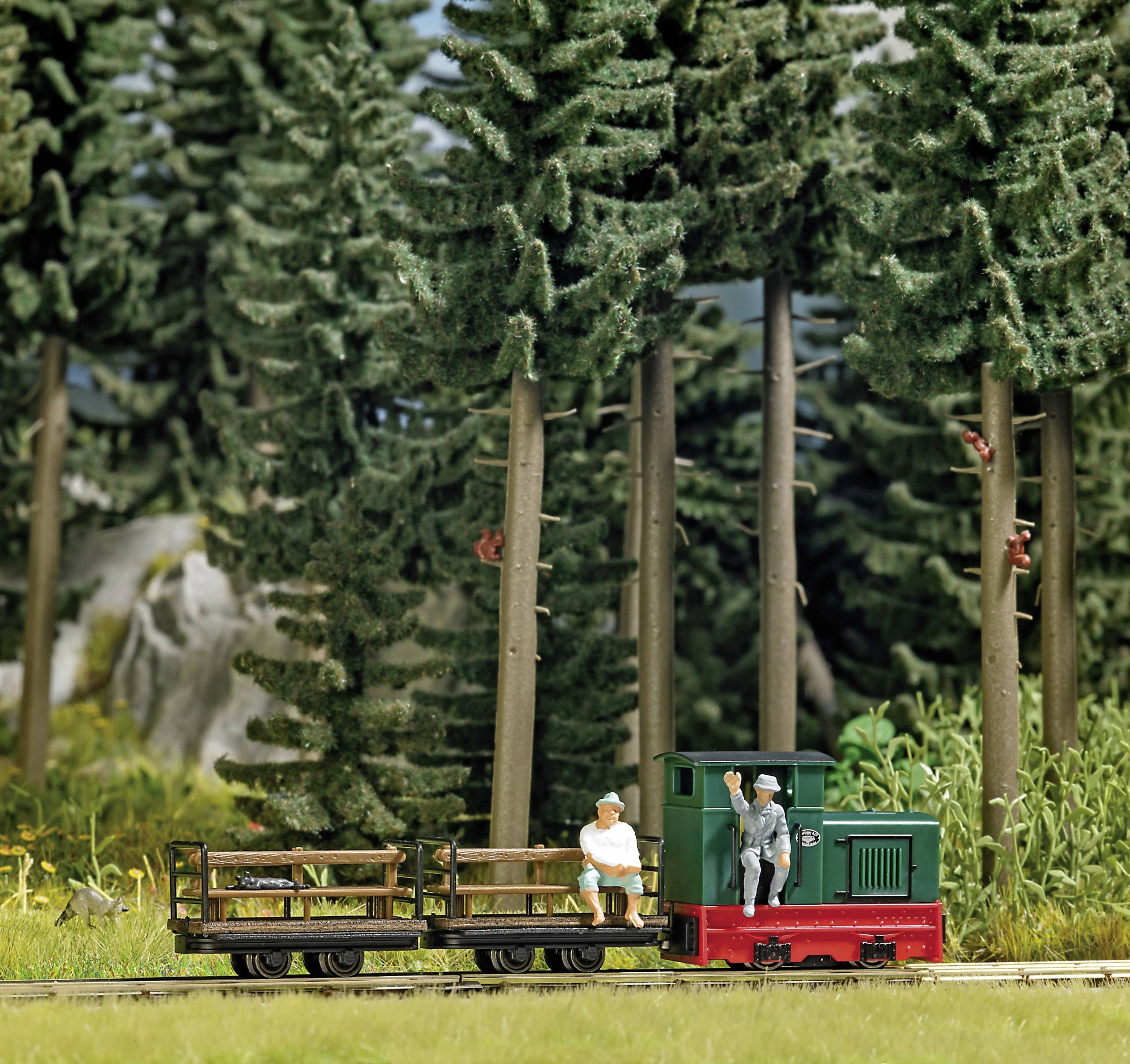 A miniature railway travels through a forest, with two figures: one sitting on a wooden crate, the other standing on the locomotive.